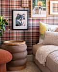 Framed pieces of art on a plaid wallpapered wall next to a fuzzy couch with decorative pillows.