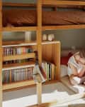 Child sitting on the floor reading under a bunk bed.