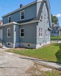 Flat, concrete area behind blue gray house with side lawn.