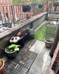 Balcony with empty flower pots, partial flooring and astroturf, and bistro set.