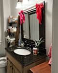 Small bathroom with a white shower curtain, dark granite sink, wooden mirror, and decorative red bows.