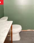 Small bathroom with dark green walls, a white toilet, and a marble countertop on a wooden vanity.