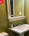 Small bathroom with green walls, white sink, mirror, towel ring, and soap dispenser.