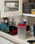 Cluttered kitchen counter with dirty dishes, bowls, and a blender near the sink, and a water bottle on the side.