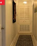 Narrow hallway with light-colored walls, a patterned runner rug, and colorful wall art.