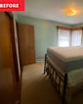 A small bedroom with a black metal bed frame, unmade mattress, and a nightstand with a lamp. Light green walls and curtains.