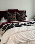 Cozy bedroom featuring a bed with tiger print pillows, a black and white throw, and a wooden nightstand with a lamp.