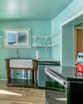 Kitchen with mint green walls, wooden flooring, a farmhouse sink, and open shelving.