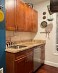 Small kitchen with wooden cabinets, granite countertop, sink, and hanging pots on a blue wall.