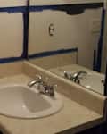 Bathroom sink with a white basin, chrome faucet, and partially painted blue walls. Mirror reflects the countertop.