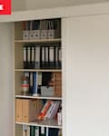 Shelving unit with binders, books, and storage boxes, featuring a sliding door on the right.