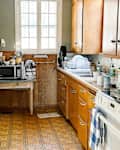 Cluttered kitchen with wooden cabinets, a white refrigerator, microwave, and dishes on the counter.