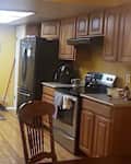 Kitchen with yellow walls, wooden cabinets, stainless steel appliances, and a small dining table with a chair.