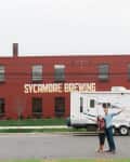 Couple standing in front of a large RV parked outside Sycamore Brewing building.