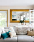 Open turquoise front door in a living room with a beige sofa, gold-framed mirror, and globe on a table.
