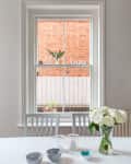 Dining table with striped bowls, candles, and a vase of white roses in front of a window with a brick wall view.