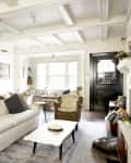 Cozy living room with white sofa, gray pillows, wooden chairs, coffee table, and fireplace, featuring a guitar on the wall.