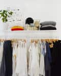 Clothing rack with assorted shirts and jackets, shelf above with folded sweaters, potted plant, and decor items.