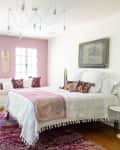 Bedroom with pink accent wall, white bed, colorful pillows, window seat, and modern chandelier.