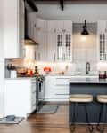 Modern kitchen with white cabinets, black fridge, marble island, and three wooden bar stools.