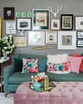 Living room with teal sofa, colorful pillows, pink ottoman, gallery wall, and decorative items on side tables.