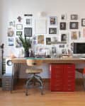 Home office with a wooden desk, red drawers, two chairs, wall art, and a computer.