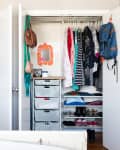Open closet with organized clothes, shoes, bags, and a small orange mirror.