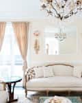 Elegant living room with beige sofa, armchairs, chandelier, and large windows with drapes.
