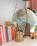 Bookshelf with children's books, a globe, a potted plant, and knitted toys on a white surface.