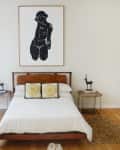 Mid-century modern bedroom with wooden bed, white bedding, abstract art, and decorative antelope sculptures on side tables.
