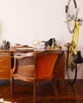 Home office with wooden desk, vintage chair, potted plants, wall art, and a yellow bike mounted on the wall.