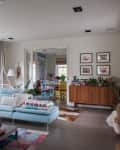Spacious living room with light blue sectional sofa, colorful cushions, and a view into a dining area with vibrant chairs.