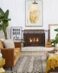 Living room with brown sofa, fireplace, large plants, guitar, and a yellow throw on a gray sectional.