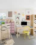 Craft room with woven wall hangings, pink drawers, yellow chair, desk with computer, and colorful framed art on walls.