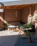 Outdoor patio with wooden walls, black cushioned seating, hanging lanterns, and a sign reading "Life is better in the garden."