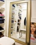 Walk-in closet with shelves of shoes, folded clothes, a large ornate mirror, and a stool.
