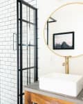 Bathroom with glass shower, white subway tiles, round mirror, and gold fixtures.