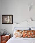 White ornate headboard with decorative pillows, framed art, and geometric decor on bedside tables.