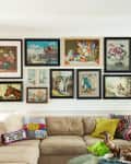 Gallery wall with eclectic framed art above a beige sectional sofa, colorful pillows, and a yellow side table with a lamp.