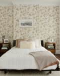 A low platform bed with a white quilt in front of an accent wall covered with muted floral wallpaper