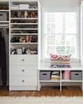 Organized walk-in closet with shelves of shoes, bags, and clothes, featuring a window seat with a colorful pillow.