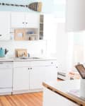 Bright kitchen with white cabinets, wooden countertops, green stools, and a chevron-patterned pendant light.