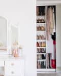 White vanity with mirror, yellow flowers, perfumes, and makeup brushes beside an open closet with shoes and clothes.
