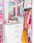 Pink closet with white dresser, colorful jewelry, and vibrant clothing, including a yellow dress and patterned shirts.
