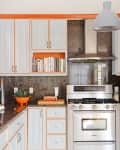 Modern kitchen with stainless steel stove, gray cabinets with orange trim, books, and an orange bowl with greens.