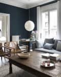 Living room with dark blue walls, gray sofa, wooden coffee table, leather chairs, and a large round pendant light.