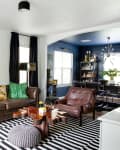 Living room with brown leather sofa, green pillows, abstract yellow art, striped rug, and adjacent dining area.