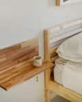 Wooden bed with white bedding, black and white pillows, and a small wooden side shelf holding a mug.