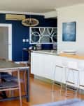 Open-plan kitchen and dining area with blue accent wall, wooden table, white bar stools, and modern decor.