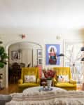 Living room with yellow armchairs, colorful cushions, a floor lamp, bookshelves, and a large wall art piece.
